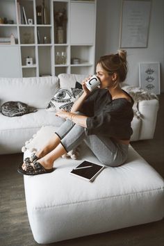 a woman sitting on top of a white couch drinking from a cup