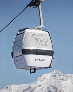 a cable car with the word chanel painted on it's side in front of snow covered mountains