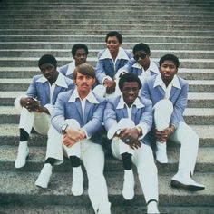 a group of men sitting next to each other in front of stairs with their hands on their hipss