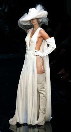 a woman in a white dress and hat on the runway