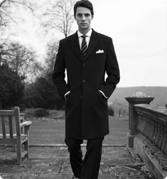 a man wearing a suit and tie standing in front of a bench