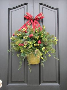 a potted plant with pine cones, berries and evergreens hangs on the front door