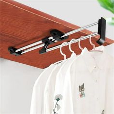 clothes hangers are hanging on the rail in front of white shirts and green plant