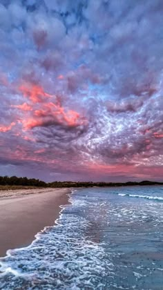 an ocean beach with waves coming in to shore and colorful clouds above it at sunset