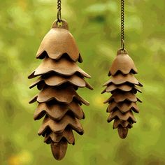 two wooden pine cones hanging from chains in front of a green background with trees and grass