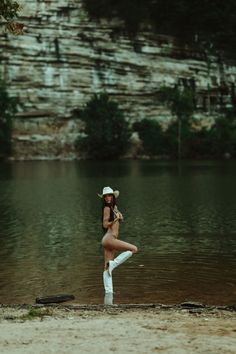 a woman is standing in the water wearing white boots and a cowboy hat with her legs crossed