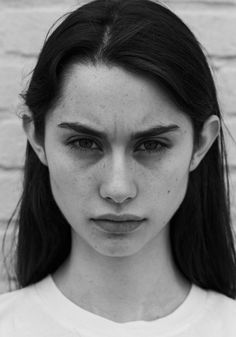 a woman with freckles on her face is looking at the camera while wearing a white t - shirt