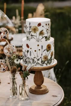 a three tiered cake sitting on top of a wooden table next to vases filled with flowers