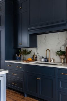 a kitchen with blue cabinets and marble counter tops, gold pulls on the faucet