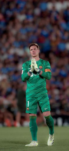 a soccer player is standing on the field with his hands folded in front of him