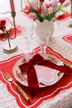 the table is set with red napkins, silverware and pink tulips