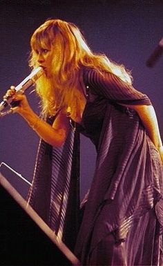 a woman with long blonde hair holding a microphone in her hand and singing on stage