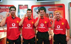 four men in red shirts are holding cell phones and talking on the same phone while standing next to each other