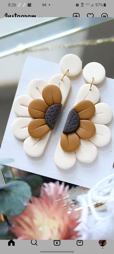 a pair of flower shaped earrings sitting on top of a white table next to flowers