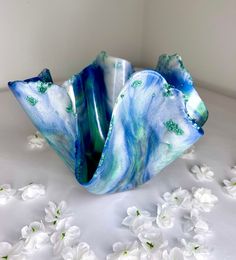 a blue and green vase sitting on top of a white table covered in flower petals