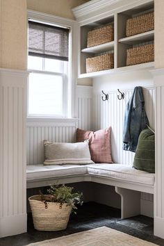 a white bench sitting under a window next to a basket filled with pillows and blankets