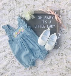 a baby's outfit and shoes are laying on a bed next to a sign that says, oh baby it's a little lady