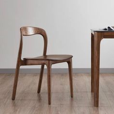 a wooden chair sitting next to a table on top of a hard wood floor in front of a white wall