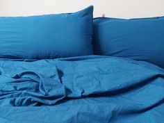 a bed with blue sheets and pillows on top of it in front of a white wall