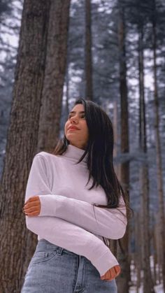 a woman standing in the middle of a forest with her arms crossed and looking off into the distance