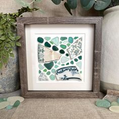 a frame with sea glass in it on a table next to some potted plants