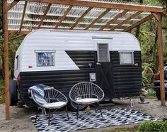 an rv is parked under a pergolated area with two chairs and a table