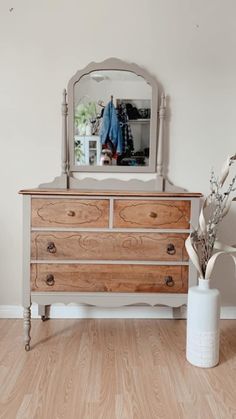 a dresser with a mirror on top of it next to a vase filled with flowers