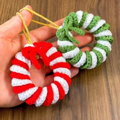 two handmade christmas wreaths are being held by someone's fingers on a wooden table