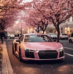 a pink car parked on the side of a road next to trees with pink flowers