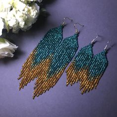 two pairs of beaded earrings sitting on top of a purple table next to flowers