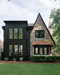 a black house with lots of windows and grass in front of the house is surrounded by trees