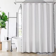 a white shower curtain with black trim in a bathroom next to a bathtub and potted plant