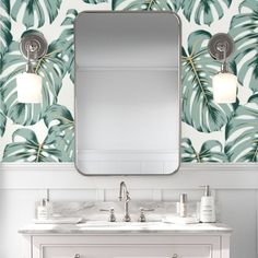 a bathroom vanity with two sinks and a large mirror above it, in front of a palm leaf wallpaper