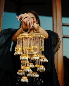 a woman is holding her hands together to show off some gold and white beads hanging from it