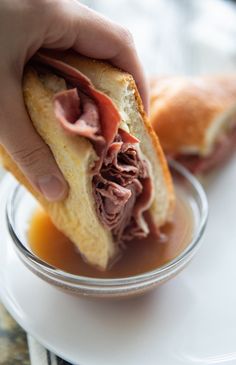 a person holding a sandwich in their left hand and dipping it into the other side