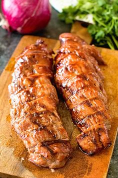 two pieces of meat sitting on top of a wooden cutting board next to an onion