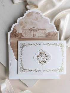 a white wedding card with an ornate design on the front and side, sitting next to a