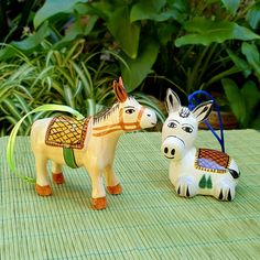 two ceramic donkeys sitting on top of a green mat next to some plants and trees