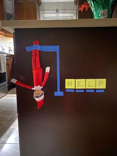 an elf is hanging upside down on a refrigerator door with the word help painted on it