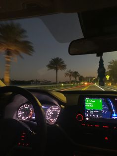 the dashboard of a car at night with palm trees and street lights in the background