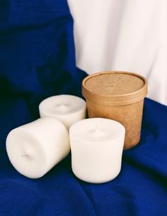 three white candles sitting next to a wooden container on a blue cloth covered tablecloth