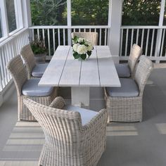 a table and chairs on a porch with flowers in the vase at the end of the table