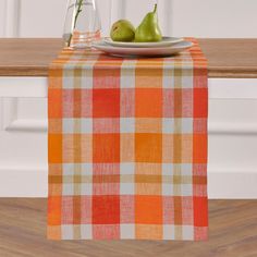 two pears are sitting on a plate next to an orange and white checkered table runner