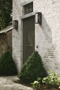 a white brick building with two green doors and some bushes in front of the door