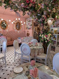 the interior of a fancy restaurant with white chairs and pink flowers hanging from the ceiling