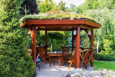 a wooden gazebo with grass on the top and chairs around it, surrounded by greenery