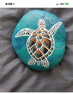 a turtle painted on a rock sitting on top of a bed next to a gray sheet