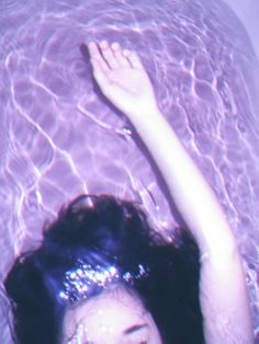 a woman with her hands up in the air above water, wearing a tiara