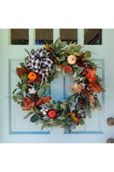 a wreath with leaves and pumpkins hanging on the front door to welcome you home