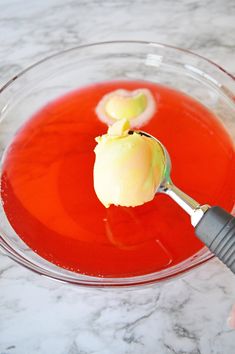 someone is spooning ice cream into a bowl of red liquid with two pieces of an apple on top